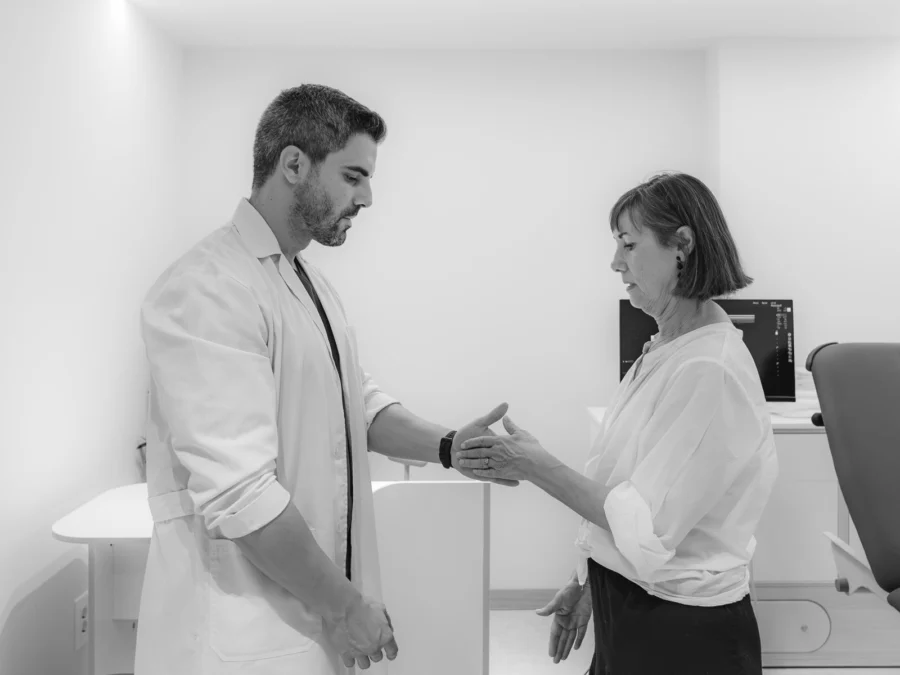 Médico explorando el hombro de una paciente, en blanco y negro
