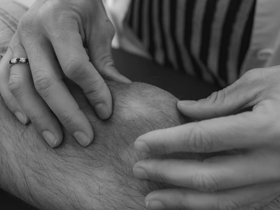 Manos de una médica explorando una rodilla, en blanco y negro