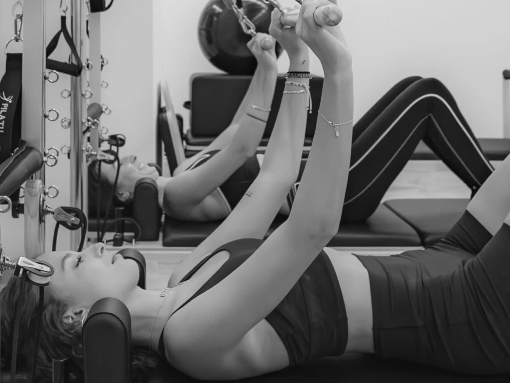 Ejercicio de pilates en reformer con los brazos elevados, en blanco y negro