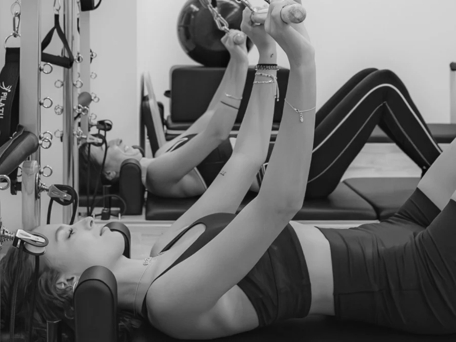 Ejercicio de pilates en reformer con los brazos elevados, en blanco y negro