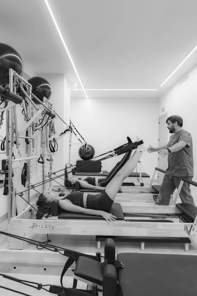 Fisioterapeuta supervisando una clase de reformer, en blanco y negro