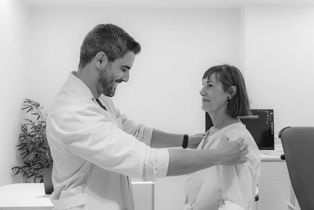 Médico explorando el hombro de una paciente, en blanco y negro
