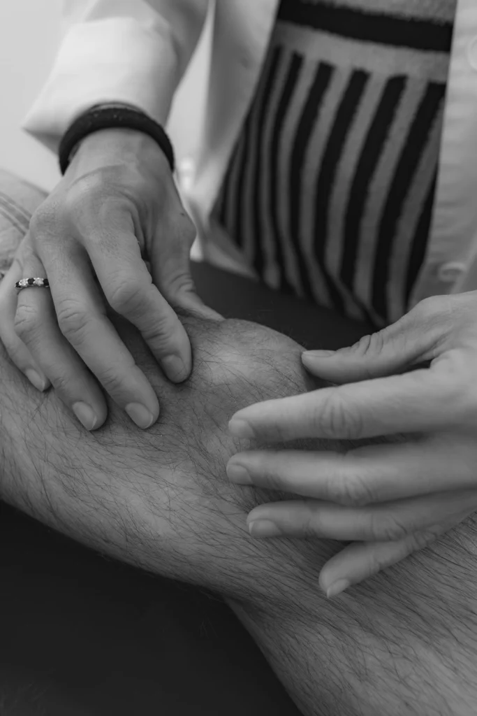Manos explorando una rodilla, en blanco y negro
