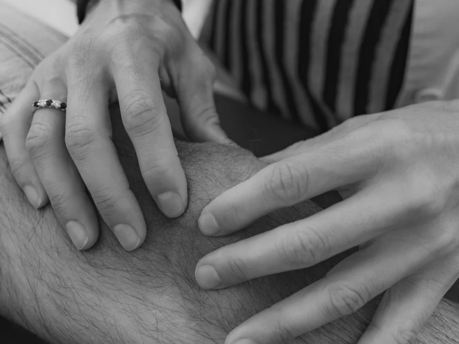 Manos explorando una rodilla, en blanco y negro